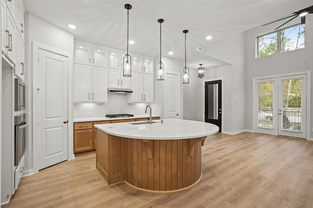 kitchen featuring a sink, an island with sink, white cabinets, and light countertops