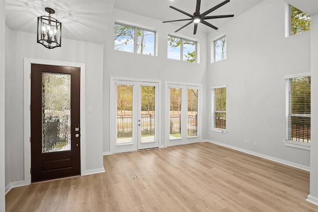 entryway with baseboards, ceiling fan with notable chandelier, a towering ceiling, and light wood-style floors