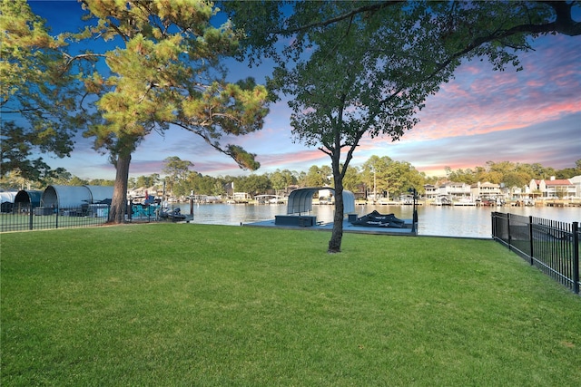 yard at dusk featuring fence, a boat dock, and a water view