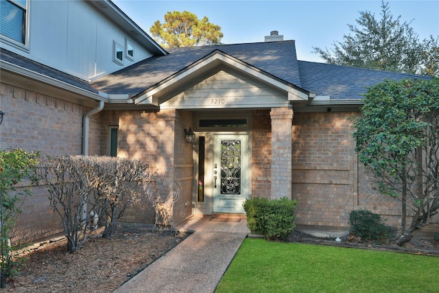 property entrance with brick siding, a shingled roof, and a chimney