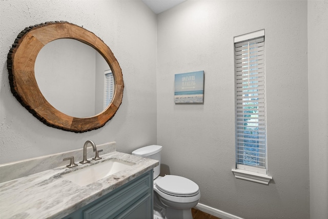 half bath with vanity, toilet, a textured wall, and baseboards