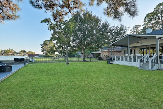 view of yard featuring fence, ceiling fan, and a water view