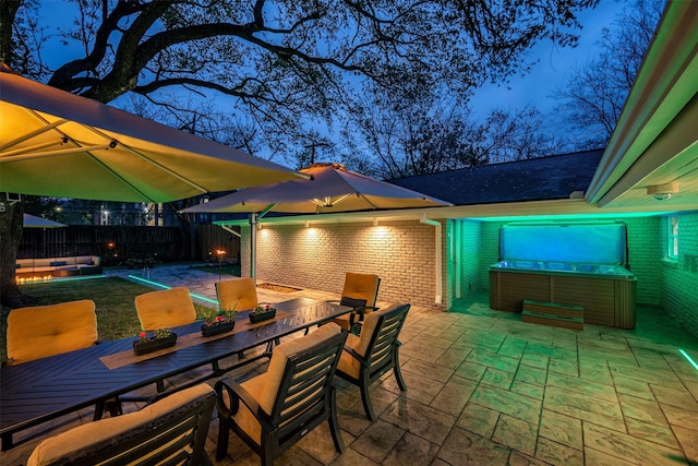 view of patio featuring a hot tub, a water view, outdoor dining area, and fence