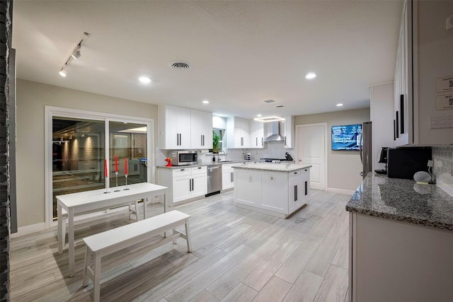 kitchen with visible vents, a center island, wall chimney exhaust hood, appliances with stainless steel finishes, and white cabinets