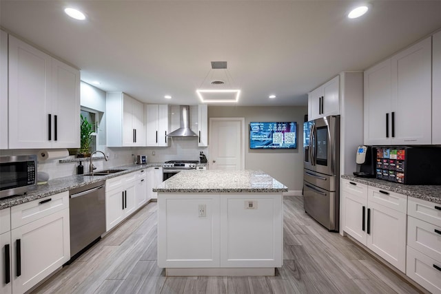 kitchen with a center island, appliances with stainless steel finishes, white cabinets, a sink, and wall chimney exhaust hood