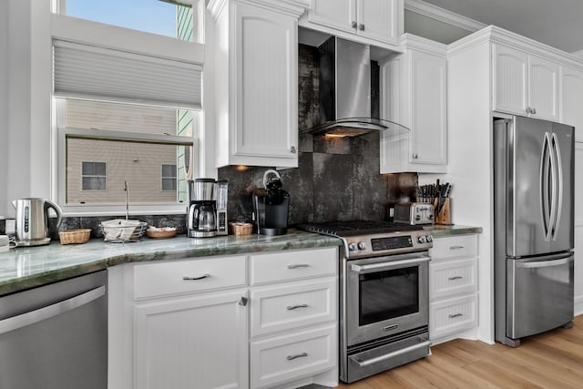 kitchen featuring light wood-type flooring, wall chimney range hood, white cabinetry, and appliances with stainless steel finishes