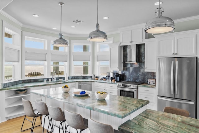 kitchen with wall chimney exhaust hood, appliances with stainless steel finishes, white cabinets, and a center island