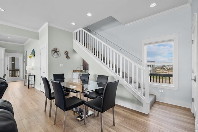 dining space with light wood-type flooring, crown molding, and stairway