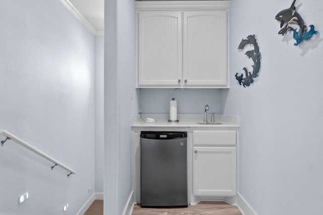 bar featuring freestanding refrigerator, indoor wet bar, a sink, and baseboards