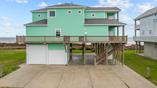 rear view of house featuring a garage, a shingled roof, a balcony, stairs, and a yard