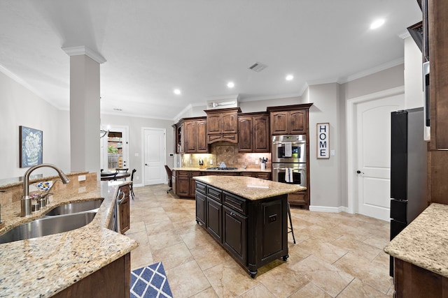 kitchen featuring a sink, light stone counters, appliances with stainless steel finishes, a center island, and dark brown cabinetry