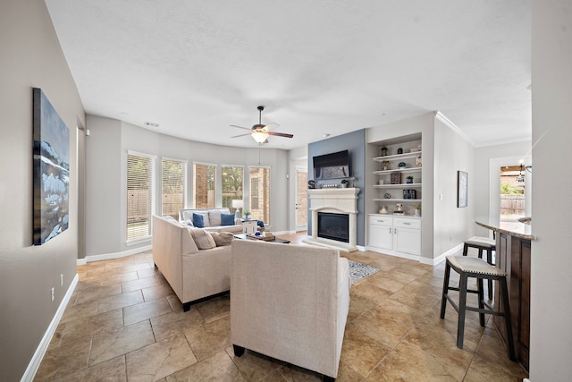 living area with a ceiling fan, baseboards, a textured ceiling, a glass covered fireplace, and built in shelves