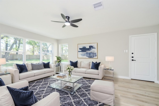 living room featuring baseboards, a ceiling fan, visible vents, and light wood-style floors