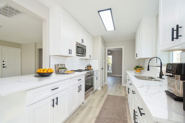 kitchen with stainless steel appliances, visible vents, a sink, white cabinetry, and light stone counters