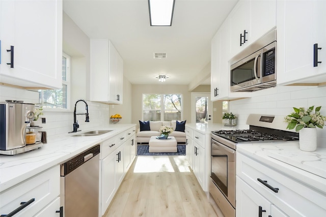 kitchen featuring appliances with stainless steel finishes, light stone countertops, visible vents, a sink, and white cabinetry