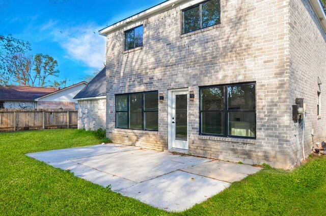 back of house with fence, brick siding, a yard, and a patio