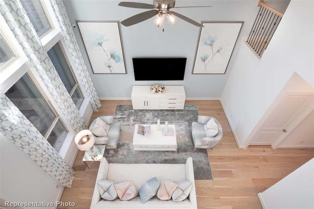 living area featuring baseboards, a ceiling fan, light wood-style floors, and a glass covered fireplace