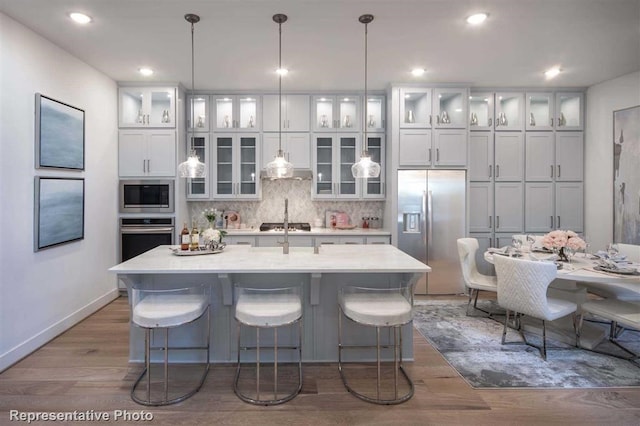 kitchen with light countertops, glass insert cabinets, hanging light fixtures, and appliances with stainless steel finishes