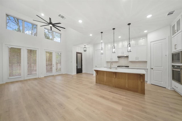 kitchen featuring a spacious island, light countertops, appliances with stainless steel finishes, white cabinetry, and glass insert cabinets