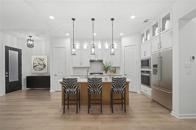 kitchen with a center island with sink, light countertops, stainless steel appliances, white cabinetry, and glass insert cabinets