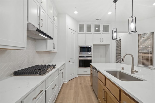 kitchen with a sink, under cabinet range hood, white cabinetry, stainless steel appliances, and glass insert cabinets