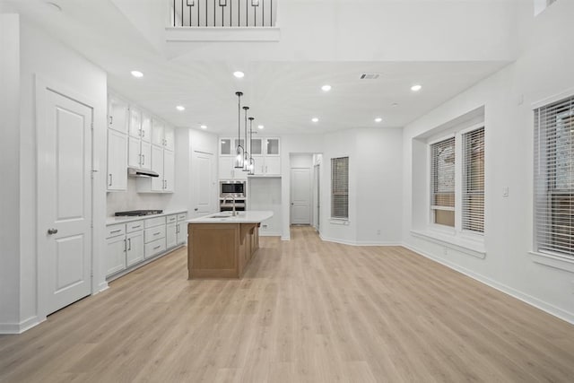 kitchen featuring a kitchen island with sink, light countertops, decorative light fixtures, white cabinetry, and glass insert cabinets