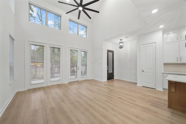 unfurnished living room with a towering ceiling, recessed lighting, a ceiling fan, baseboards, and light wood-style floors