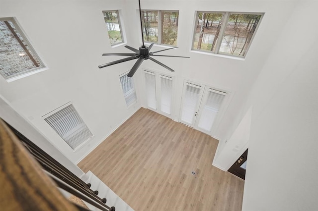 unfurnished living room featuring wood finished floors, baseboards, visible vents, ceiling fan, and a towering ceiling