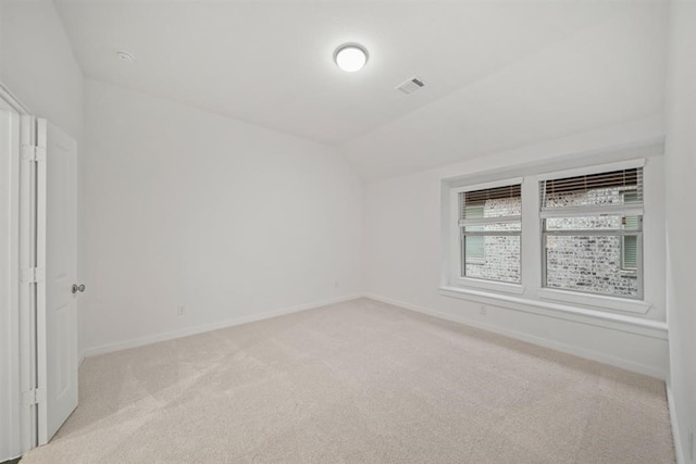 unfurnished room with baseboards, visible vents, lofted ceiling, and light carpet