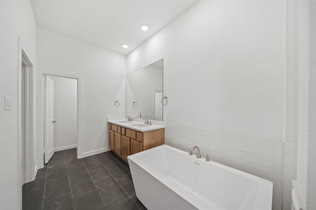 bathroom with double vanity, tile walls, recessed lighting, a sink, and a soaking tub