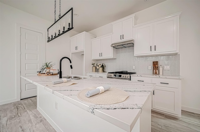 9418 Madera Rd, Houston, TX 77078 - kitchen with under cabinet range hood, a sink, stainless steel range with gas stovetop, an island with sink, and white cabinetry