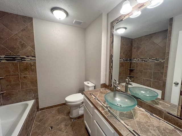 full bath featuring tiled bath, visible vents, toilet, a textured ceiling, and vanity