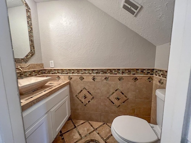 bathroom featuring toilet, visible vents, tile walls, and vanity