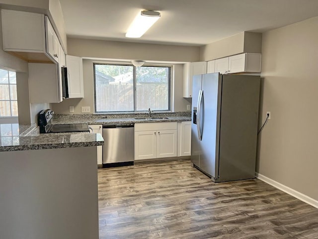 kitchen with dark wood finished floors, appliances with stainless steel finishes, white cabinets, a sink, and baseboards