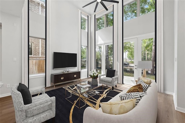 living area featuring ceiling fan, baseboards, a high ceiling, and wood finished floors