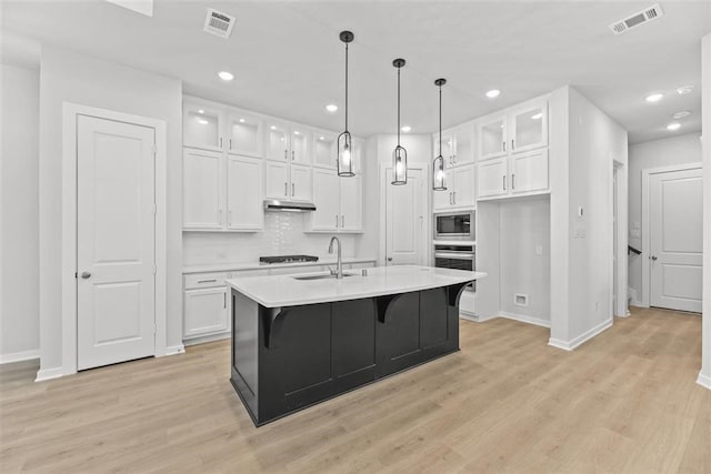 kitchen featuring visible vents, under cabinet range hood, built in microwave, stainless steel oven, and a sink