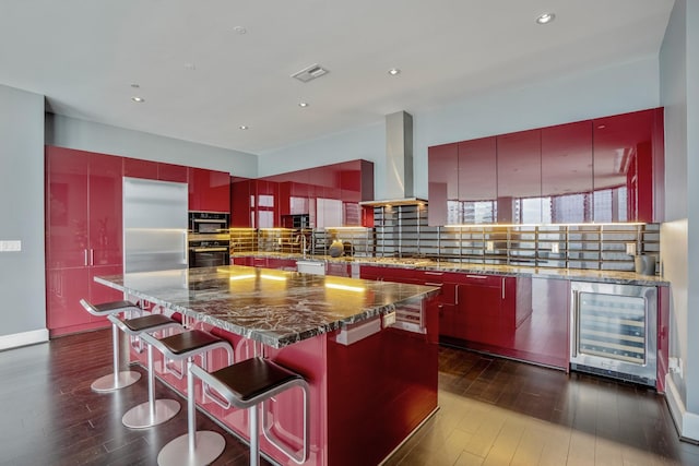 kitchen featuring modern cabinets, beverage cooler, black oven, and ventilation hood