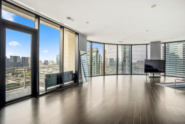 unfurnished living room with a wealth of natural light, a wall of windows, visible vents, and wood finished floors