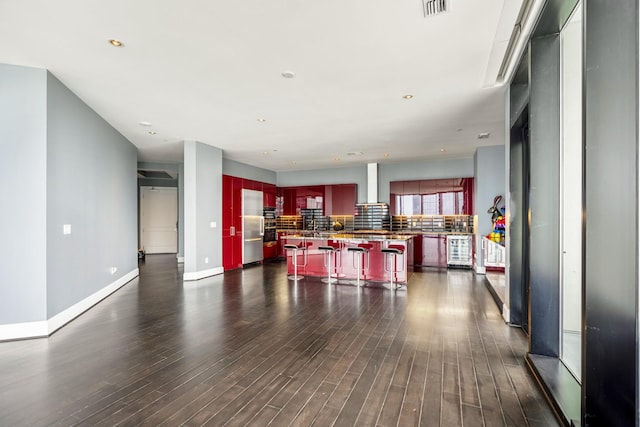 kitchen with a kitchen island, reddish brown cabinets, wall chimney exhaust hood, a breakfast bar, and stainless steel refrigerator