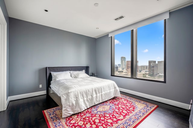 bedroom with baseboards, visible vents, a view of city, and dark wood-style floors