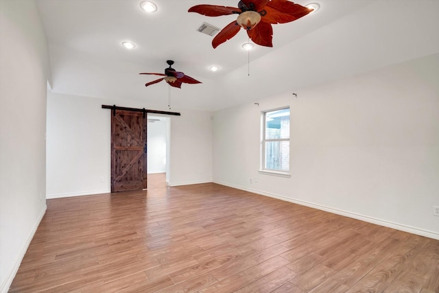 empty room featuring visible vents, light wood finished floors, baseboards, a barn door, and ceiling fan