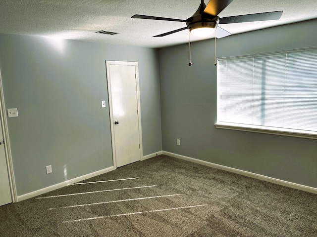 spare room with a textured ceiling, ceiling fan, visible vents, baseboards, and dark colored carpet