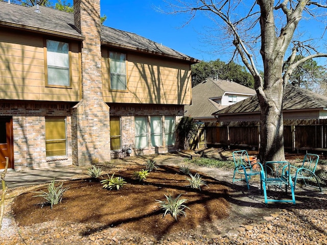 back of house with brick siding, a chimney, a shingled roof, a patio area, and fence