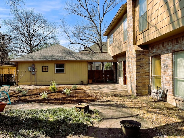 view of side of property featuring a shingled roof, brick siding, and fence