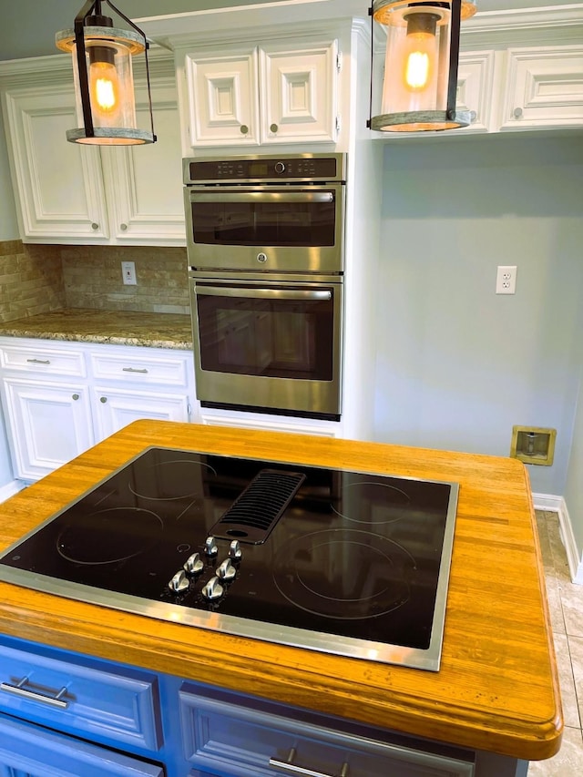 kitchen featuring double oven, black electric stovetop, white cabinets, backsplash, and pendant lighting