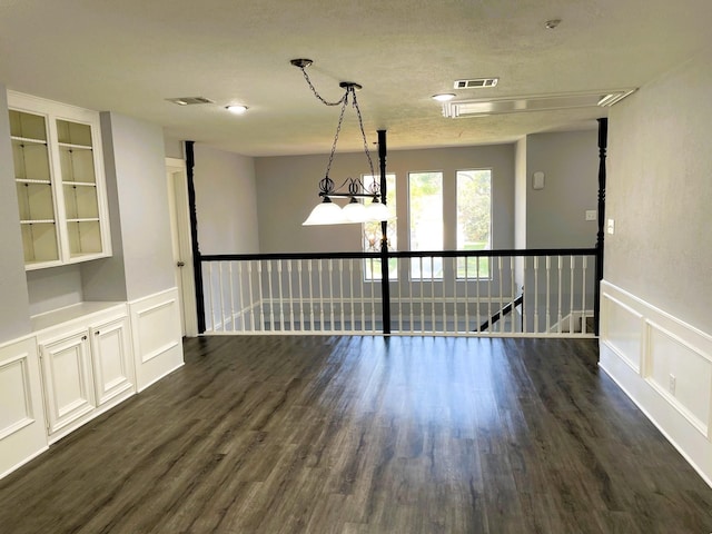 empty room with dark wood-style floors, visible vents, a decorative wall, and wainscoting