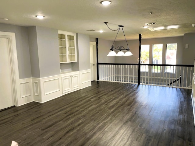 spare room featuring visible vents, dark wood finished floors, a wainscoted wall, a textured ceiling, and a decorative wall