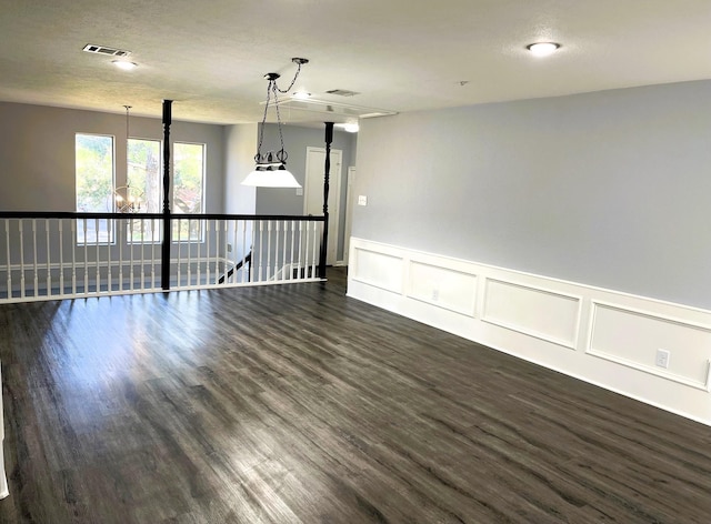 unfurnished room featuring a textured ceiling, dark wood finished floors, visible vents, and a decorative wall