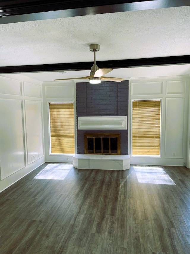 unfurnished living room featuring dark wood finished floors, a fireplace, a decorative wall, a textured ceiling, and beamed ceiling