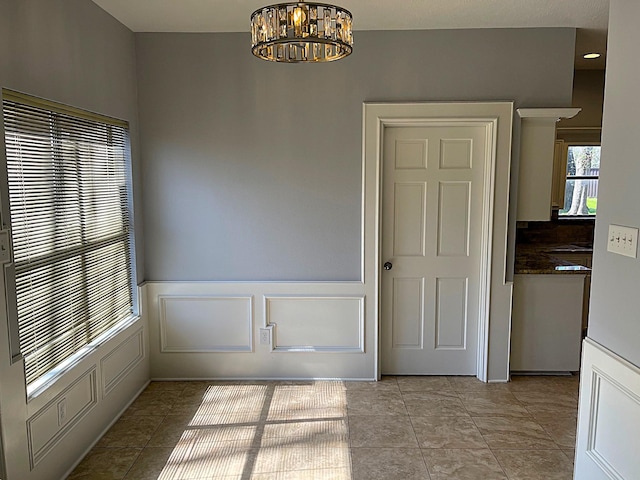 unfurnished dining area with light tile patterned flooring, a decorative wall, a notable chandelier, and wainscoting